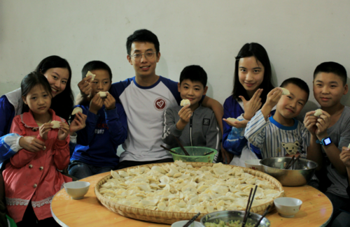 x支教团成员和孩子们在展示包好的饺子.png